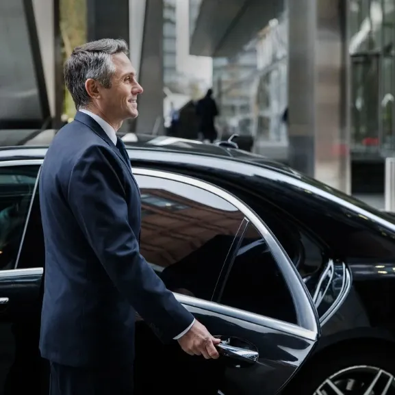 A professional chauffeur is opening luxury car door for clients.