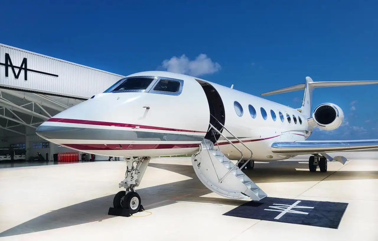 White and maroon private jet with stairs extended on the tarmac outside a hangar.