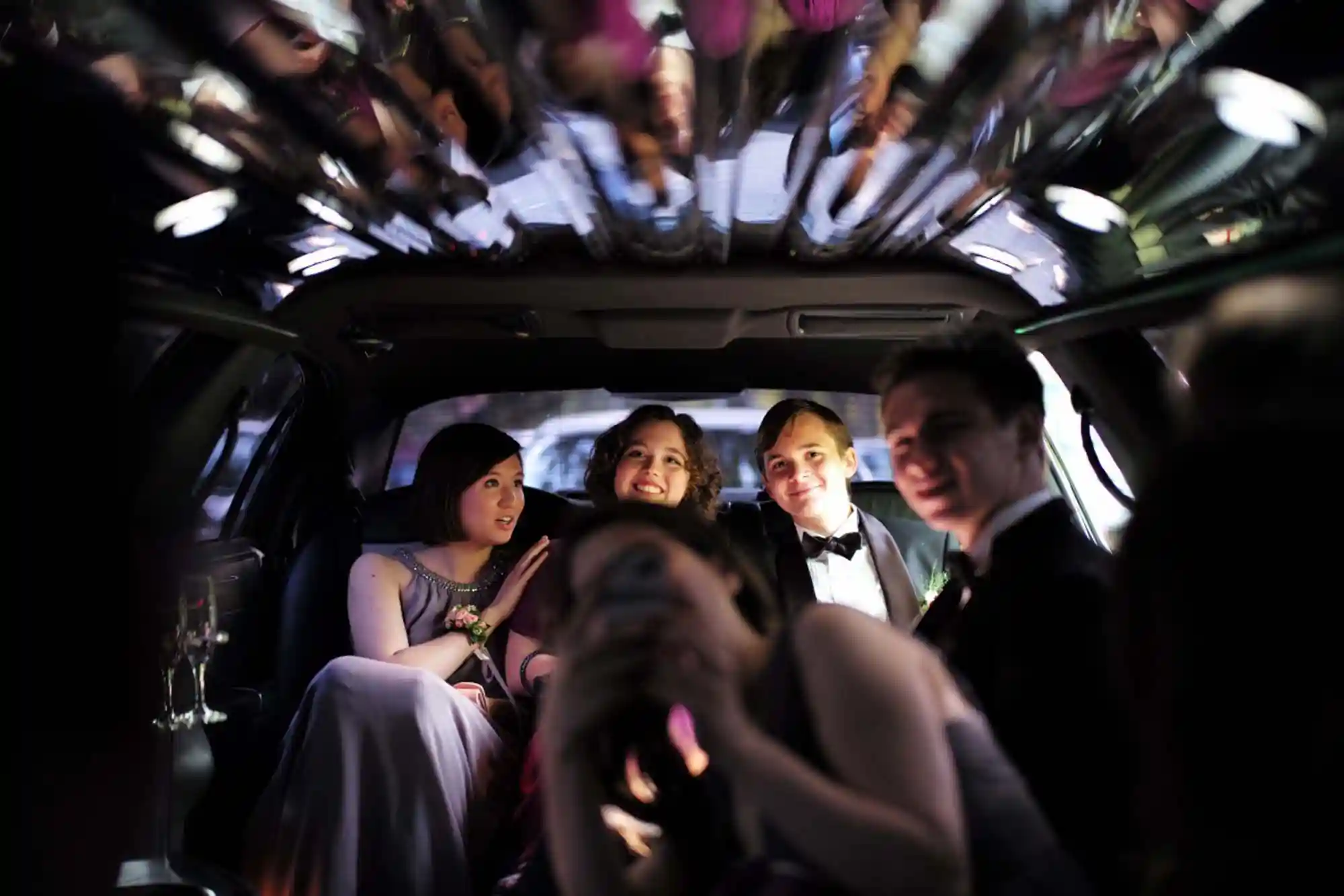 prom-limo-service Four students dressed in formal wear smiling inside the backseat of a limousine.