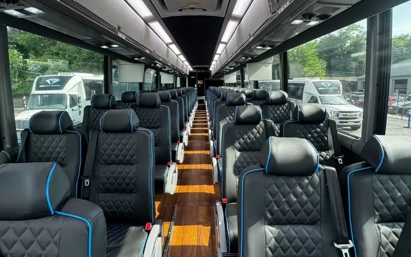 Premium 56 PAX Motor Coach interior with black quilted leather seating and wood-grain flooring
