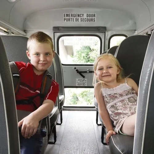 Two young children smiling while seated on a school busr Two young children smiling while seated on a school busr