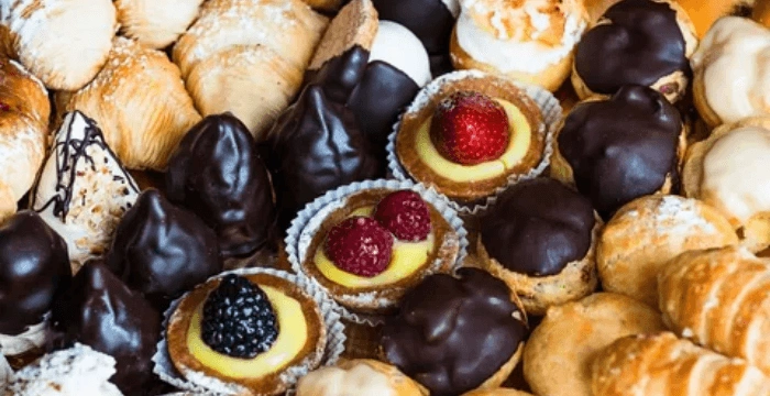 Assorted pastries and desserts, including chocolate-covered treats, cream tarts with berries, and croissants.