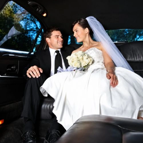 Bride and groom smiling together inside a luxury wedding limousine.