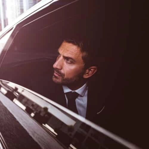 businessman wearing suit and tie looking out window of luxury car