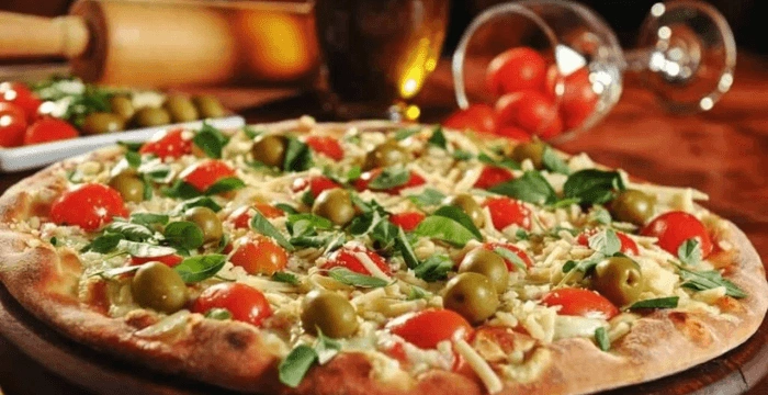 Close-up of a freshly baked pizza topped with cherry tomatoes, green olives, basil, and melted cheese.