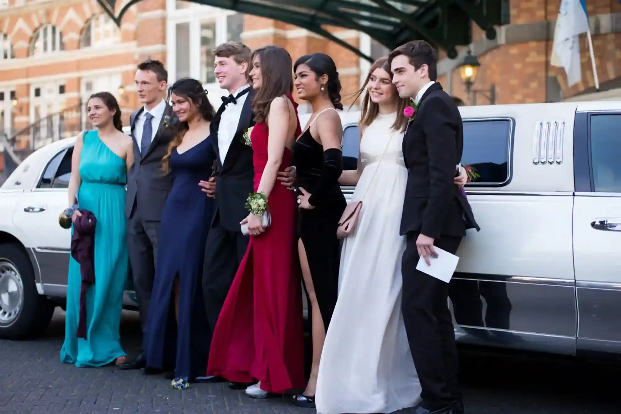Students dressed for prom standing beside a white limousine