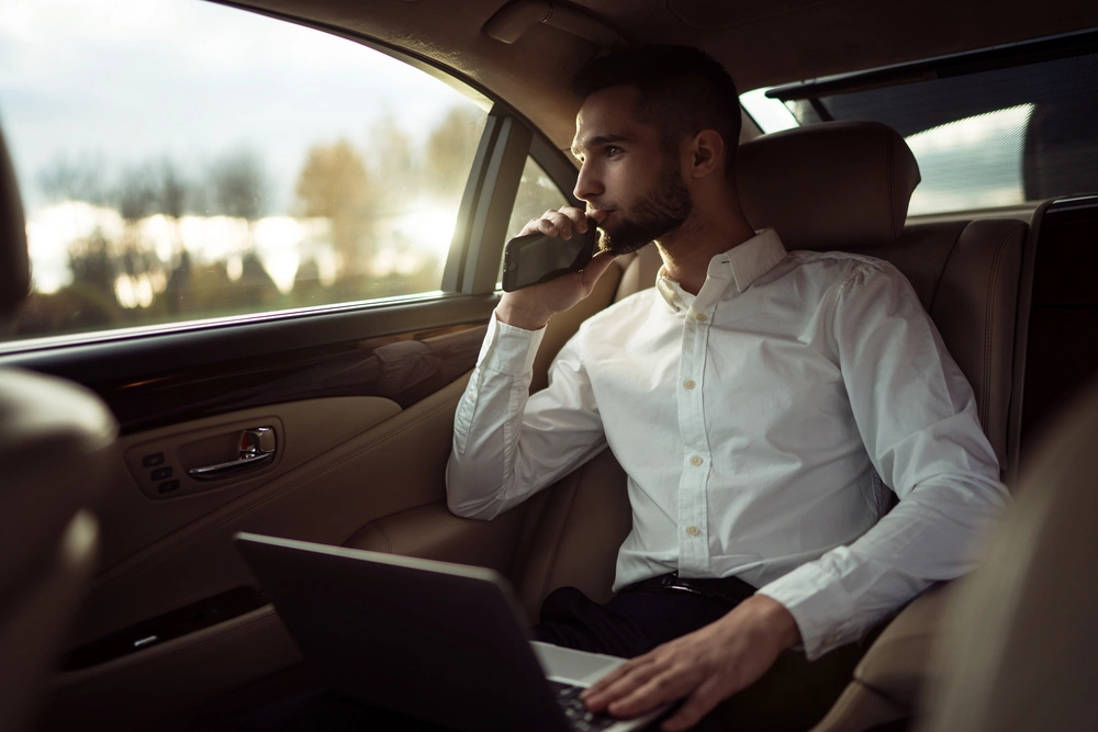 man using phone and laptop inside private car in natick ma Man using his phone and laptop inside a private car in Natick MA